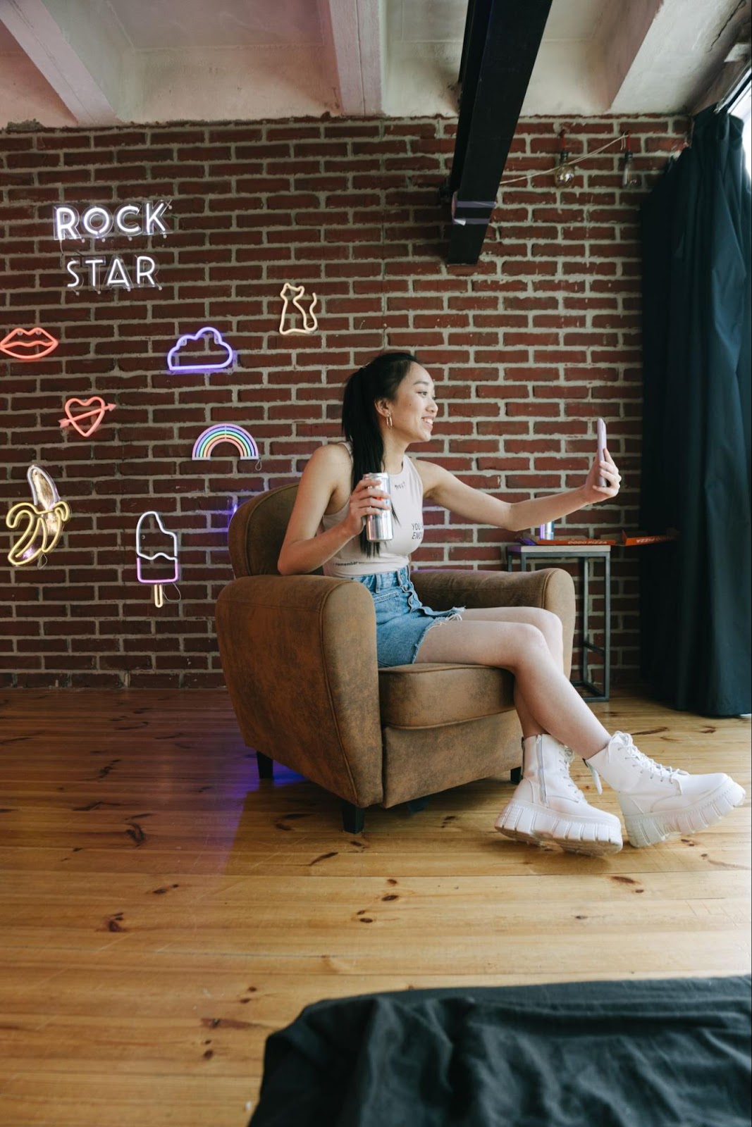 An image of a girl sitting with a phone in one hand and a drink in another